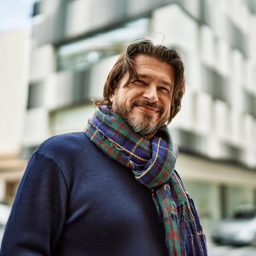 A man is dressed in a coat and scarf and is smiling.