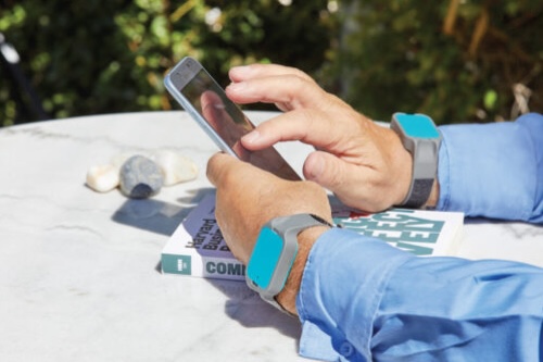 A pair of hands rests on a table, using a smartphone.
