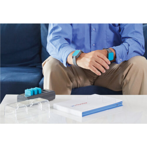 A man sits on a sofa, wearing monitoring devices on his wrists.